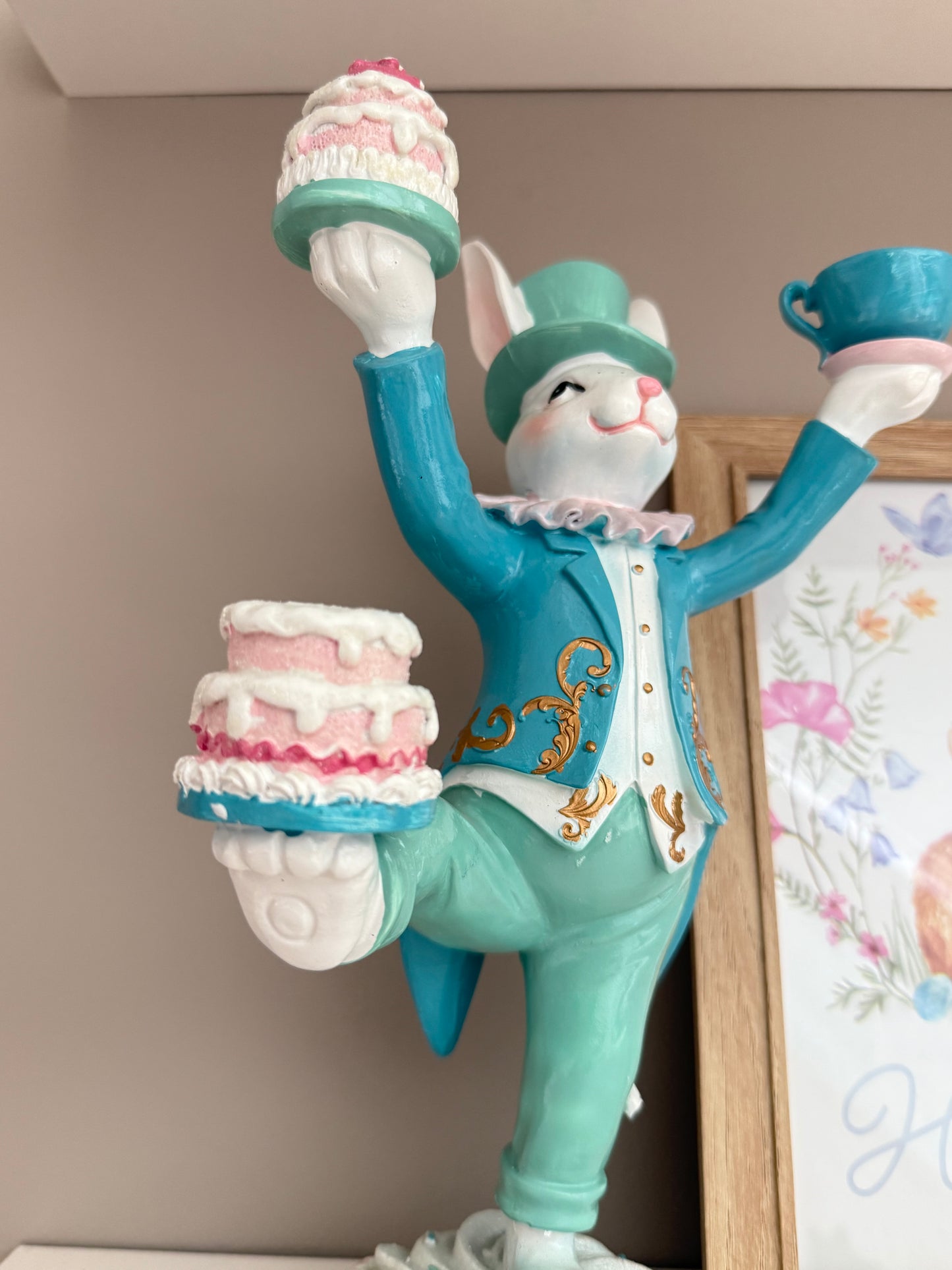 Rabbit wearing a blue coat and top hat while balancing tiered cakes and a teacup.